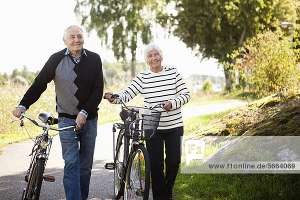 Senior couple walking with bicycles in park