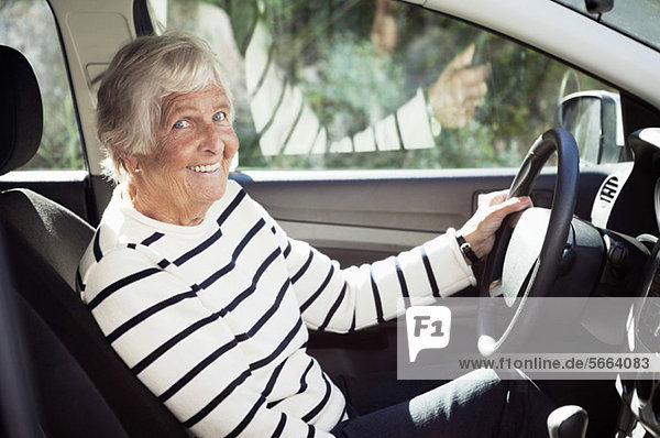 Cheerful senior woman sitting on driver seat in car