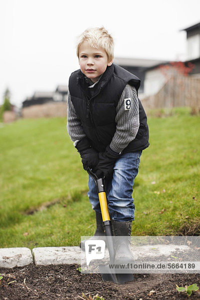 Young boy in back yard garden using shovel