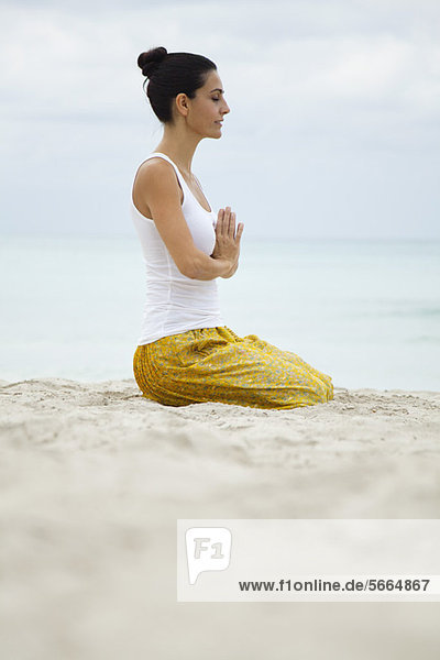 Mature woman kneeling in prayer position on beach  side view