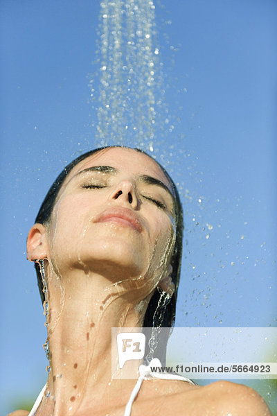 Mid-adult woman under shower outdoors with eyes closed