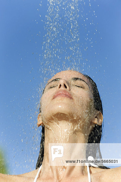 Mittlere erwachsene Frau unter der Dusche im Freien mit geschlossenen Augen