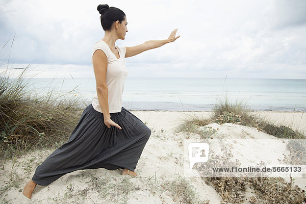 Woman practicing tai chi chuan on beach  side view