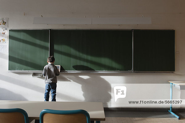 Junge steht im Klassenzimmer  vor der Tafel  Rückansicht