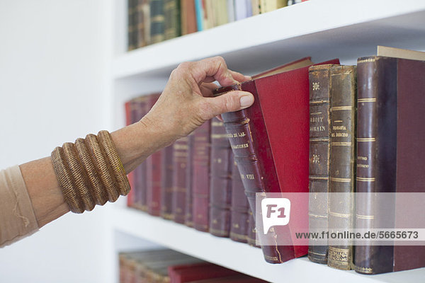 Frau wählt Buch aus dem Bücherregal  beschnitten