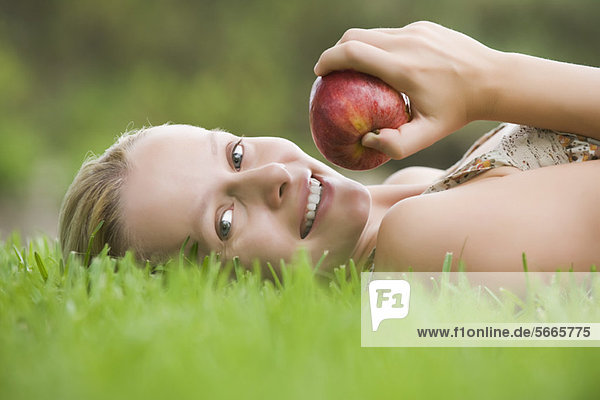 Junge Frau auf Gras liegend  Apfel haltend