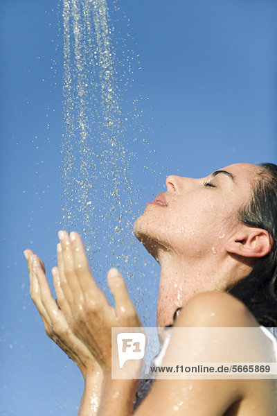 Mid-adult woman under shower outdoors with eyes closed