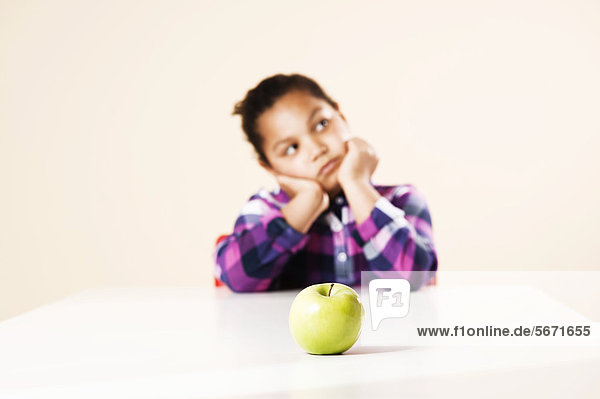 Mädchen sitzt am Tisch mit einem Apfel