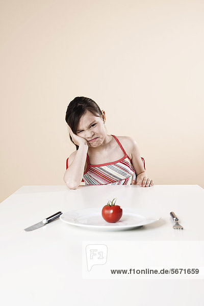 Schmollendes Mädchen sitzt am Tisch mit einer Tomate