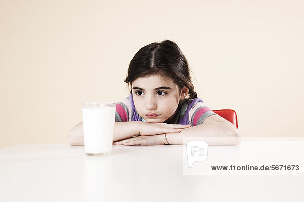 Mädchen sitzt am Tisch mit einem Glas Milch