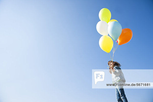 Mädchen steht mit Luftballons unter blauem Himmel