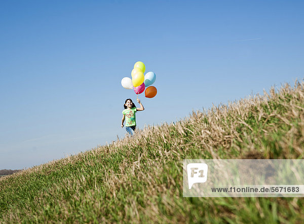 Mädchen rennt mit Luftballons auf einer Wiese