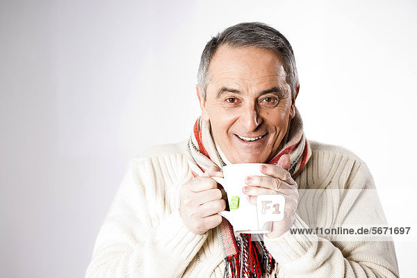 Fröhlicher Senior in Winterkleidung trinkt eine Tasse Tee