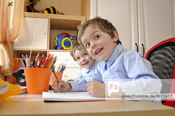 Zwillinge  Jungen  4 Jahre  sitzen am Schreibtisch und malen