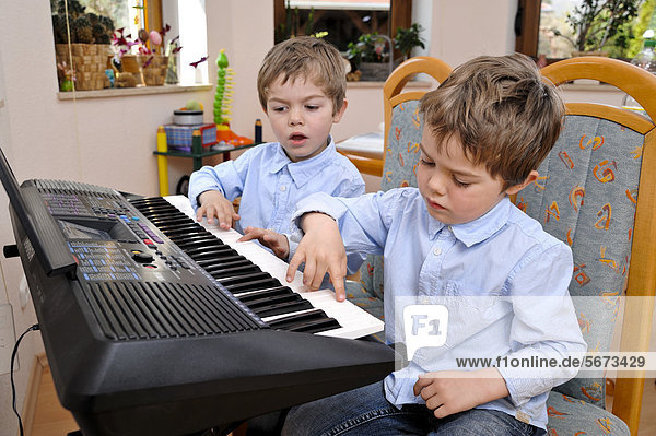 Zwei Zwillinge  Jungen  4 Jahre  machen gemeinsam Musik auf einem Keyboard