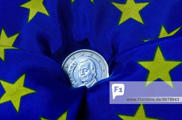 Spanische Euromünze versinkt in einer Europa-Fahne  Symbolbild