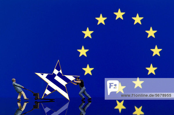 Zwei Lagerarbeiter  Miniaturfiguren  schieben einen Stern mit griechischer Flagge weg  Symbolbild Eurokrise