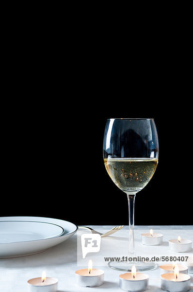 Glas Weißwein und Teelichter auf dem Tisch