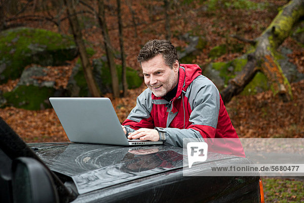 Erwachsener Mann mit Laptop an der Motorhaube