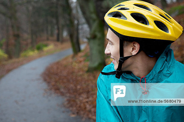 Junger Mann mit Fahrradhelm auf Waldweg und Blick über die Schulter