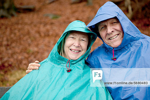 Portrait of senior couple sitting on park bench wearing waterproofs