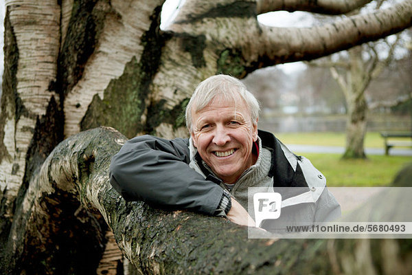 Senior man leaning against tree  smiling