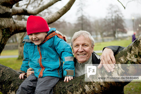 Granfather and boy sitting on tree branch  smiling