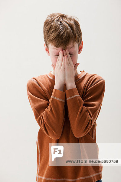 Junge in braunem Pullover reibt die Augen  Studioaufnahme