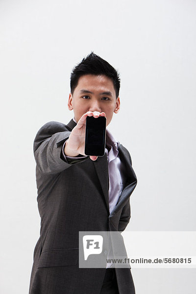 Junger asiatischer Geschäftsmann hält Handy  Studioaufnahme