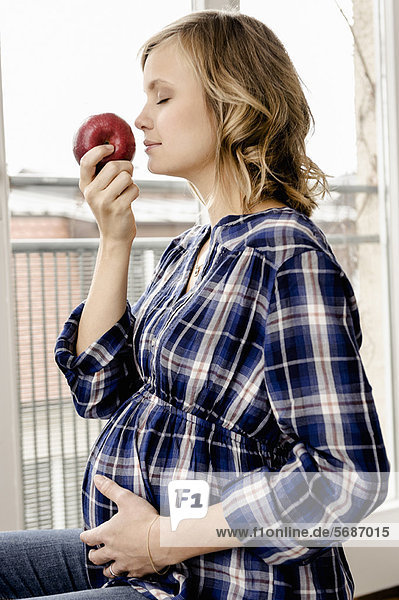 Lächelnde schwangere Frau riecht Apfel