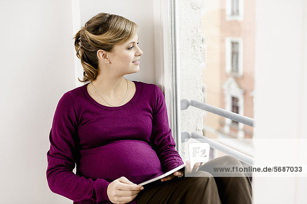 Schwangere Frau im Fenster sitzend