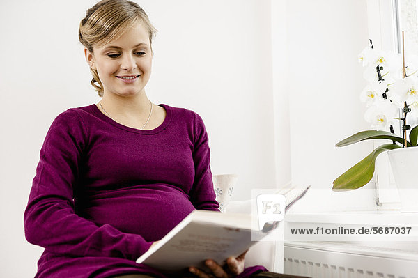 Schwangere lesend im Wohnzimmer