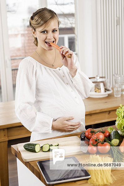 Schwangere Frau isst Karotte in der Küche