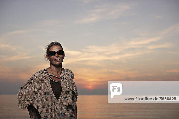 Frau steht am Strand bei Sonnenuntergang