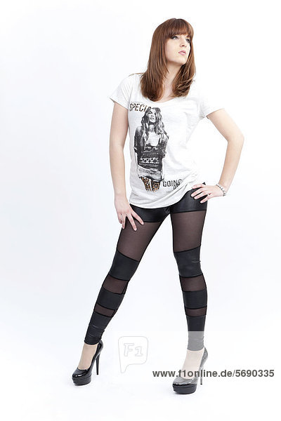 Junge Frau mit weißem Top  dunklen Leggins und High Heels posiert selbstbewusst
