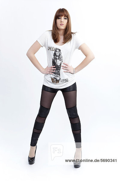 Junge Frau mit weißem Top  dunklen Leggins und High Heels posiert selbstbewusst