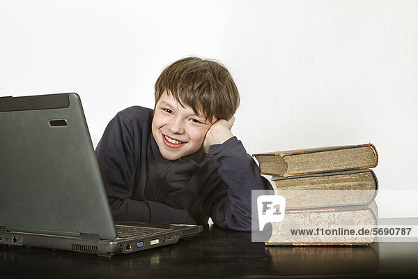 Junge mit Laptop und Bücherstapel