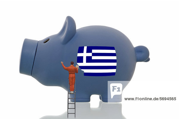 Miniaturfigürchen überstreicht Griechenland-Flagge auf blauem Sparschwein  Symbolbild