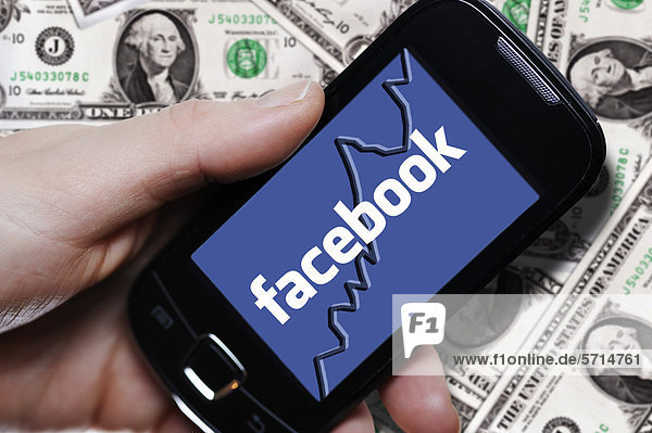 Hand mit Smartphone und Facebook-Logo vor Dollarnoten  Symbolbild Börsengang von Facebook