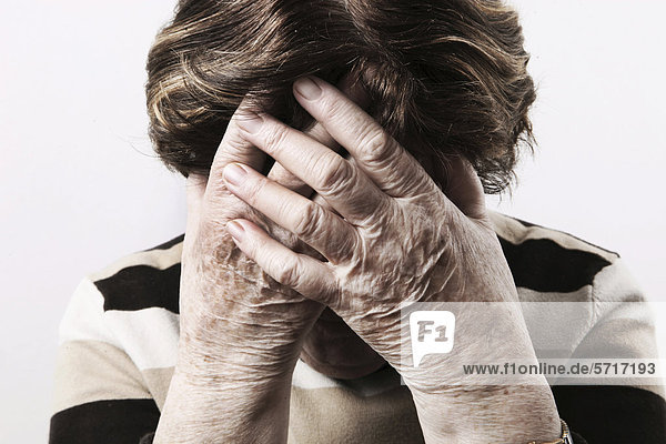 Elderly woman looking distressed and holding her hands over her face