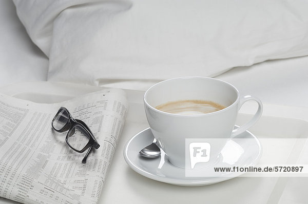 Tablett mit Kaffee mit Zeitung und Brille auf dem Bett  Nahaufnahme
