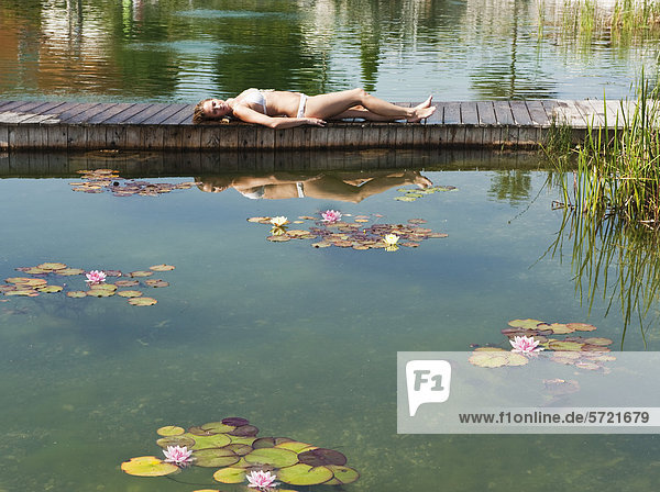 Österreich  Salzburger Land  Junge Frau auf Brücke am Pool liegend