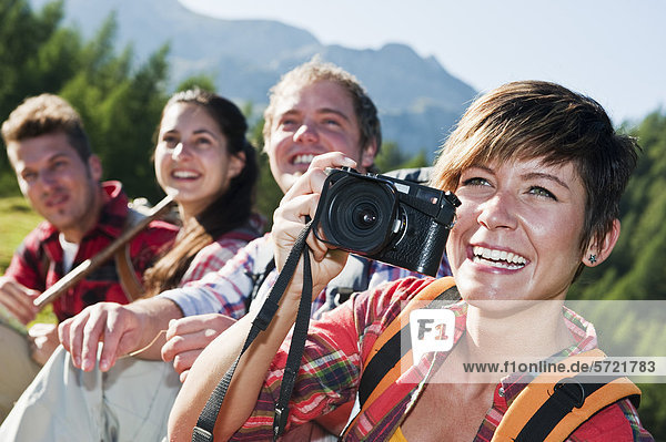 Austria  Salzburg County  Men and women sitting in alpine meadow  woman holding camera