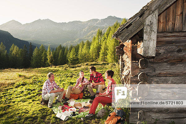 Austria  Salzburg County  Men and women having picnic near alpine hut at sunset
