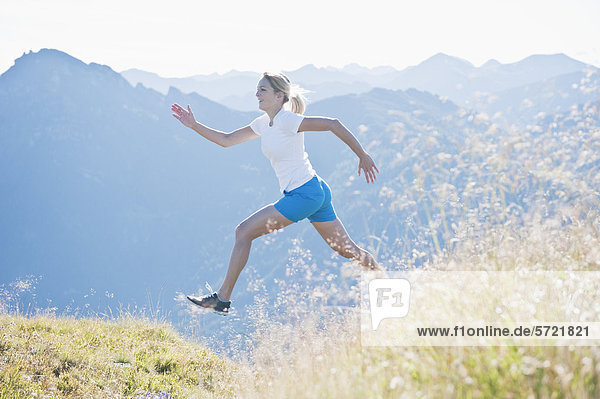 Austria  Salzburg County  Young woman running and jumping in alpine meadow