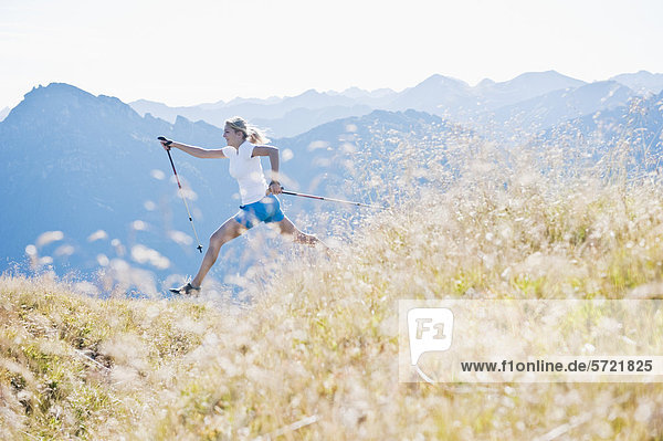 Austria  Salzburg County  Young woman with nordic walking pole and jumping in alpine meadow