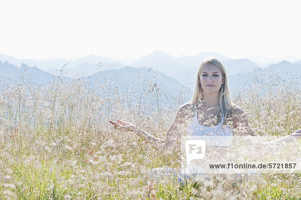 Austria  Salzburg County  Young woman sitting in alpine meadow and doing meditation