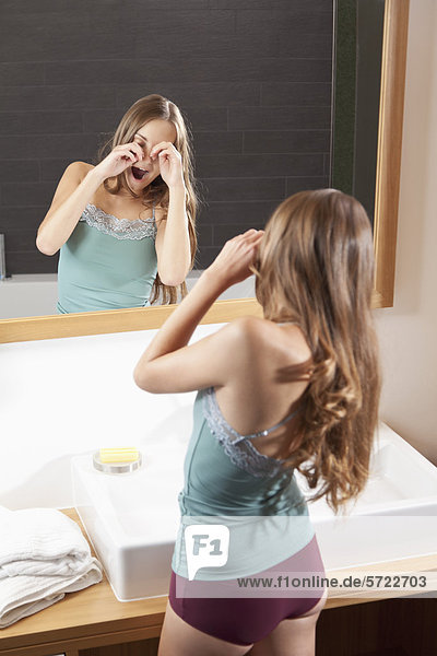 Young woman rubbing eyes in front of bathroom mirror