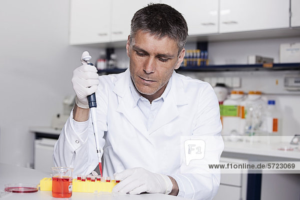 Deutschland Bayern München Wissenschaftler gießen rote Flüssigkeit mit Pipette in Reagenzglas für die medizinische Forschung im Labor