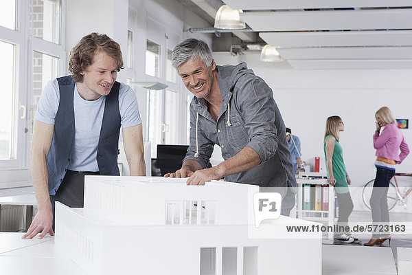 Men watching architectural model in office  colleagues talking in background